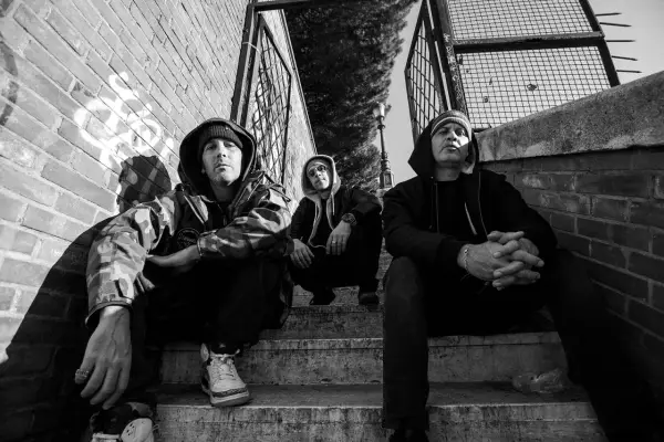 Tre uomini con cappuccio siedono sulle scale, un'atmosfera da musica hip hop famosa.